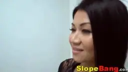 MILF asiática de pie junto a un hombre negro en el sofá