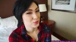 Woman in red plaid shirt laughs on the edge of the bed