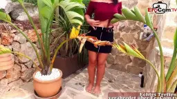 Alice stands naked with spread legs in front of tropical leaves