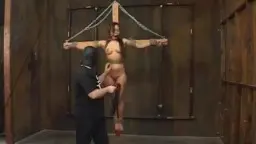 Asiática atada a la cruz de madera, hombre de negro a su lado