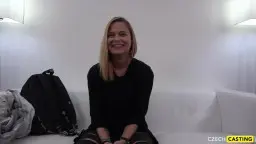 Young blonde sits smiling on white sofa, backpack beside her